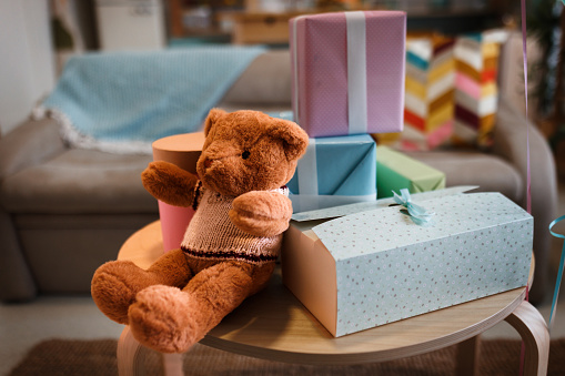 Teddy bear with gifts arranged on coffee table for baby shower party with no people