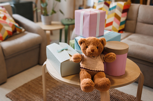 Teddy bear with gifts arranged on coffee table for baby shower party with no people