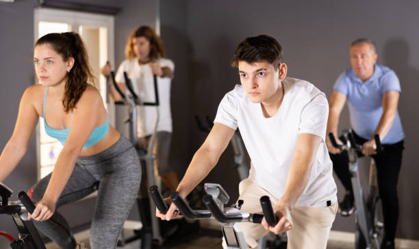 jeune homme faisant de l’entraînement cardio sur un vélo d’appartement au gymnase - cycling bicycle occupation men photos et images de collection