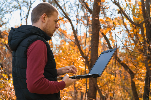 A freelance man works remotely in nature in the autumn forest. Country life. A break from civilization. Van Lifevibes. A man with laptop. Distance learning in the fresh air via a laptop. Remote work.