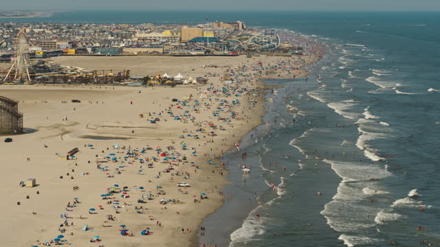 Amusement parks with rollercoasters and other attractions on the sandy beach in Wildwood, Jersey Shore, New Jersey, on a sunny day. Aerial video with backward camera motion.
