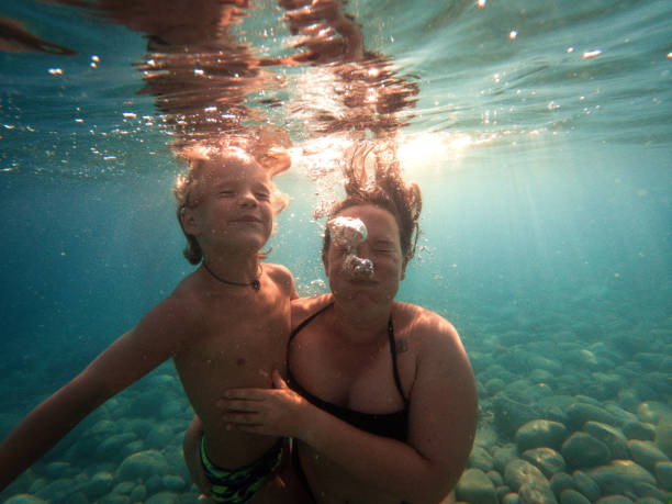 Underwater Shot of Caucasian Son and Mother Under the sea view of family having fun. Caucasian boy and mother wearing swimsuits and holding breath underwater. scuba diving family stock pictures, royalty-free photos & images