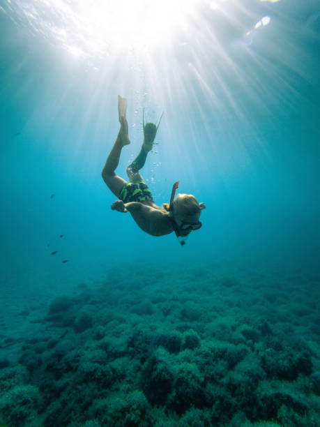 Explorer Kid nadando no oceano enquanto olha para as rochas - foto de acervo