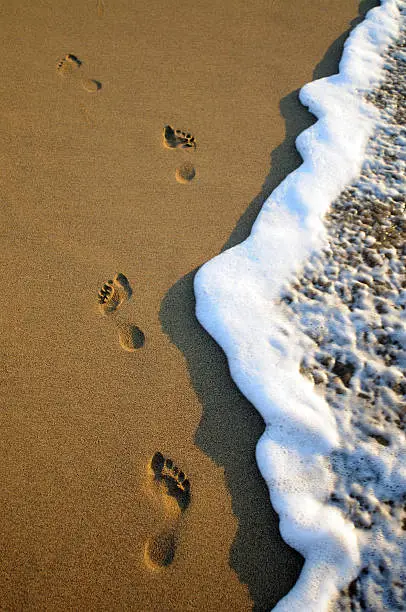 Female footsteps on the sand as a wave breaks