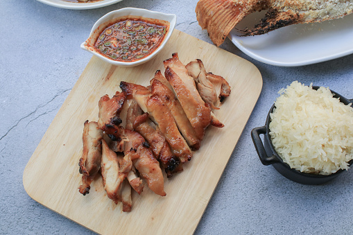 Grilled pork neck with dipping spice sauce and sticky rice on white table. Local Thai street food style