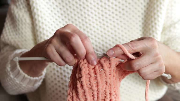 Close-up of woman's hands knitting a woolen scarf. A woman knits from thick yarn. Handmade clothes. A woman is engaged in her hobbies. Knitting concept