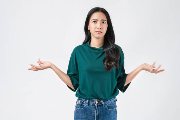 Confused young woman wearing casual green t-shirt and shrugging shoulders, isolated on white background. stock photo
