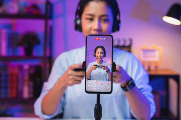 Vlogger live streaming podcast review on social media, Young Asian woman use microphones wear headphones with smartphone record video. Content creator concept. stock photo