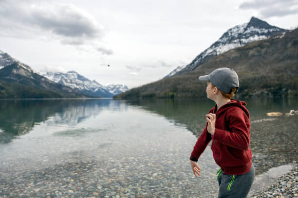 menino ruivo jogando pedras no lago waterton no verão - throwing stone little boys child - fotografias e filmes do acervo