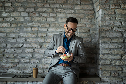 Cheerful young businessman eating a healthy salad on a work break in his office.