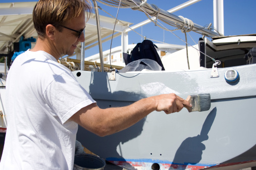 The man works on his sailboat, paints the base color on the body of the boat.