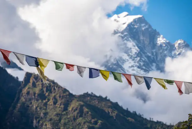 Photo of Prayer flags blowing in the wind with snowcapped mountain in background.