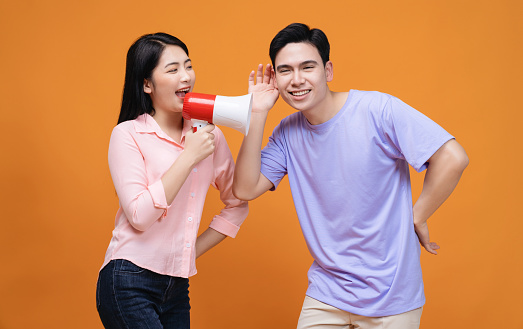 Young Asian couple with megaphone on background