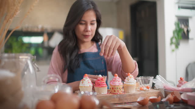 Woman sprinkles toppings on cupcakes.