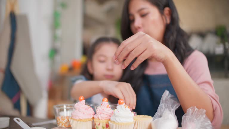 Mother and daughter sprinkle toppings on cupcakes.