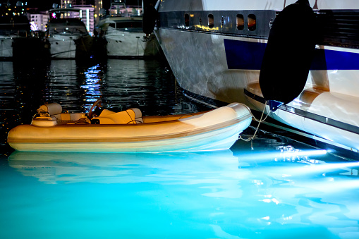 A rubber boat is moored to a yacht in the seaport. Night Scene.