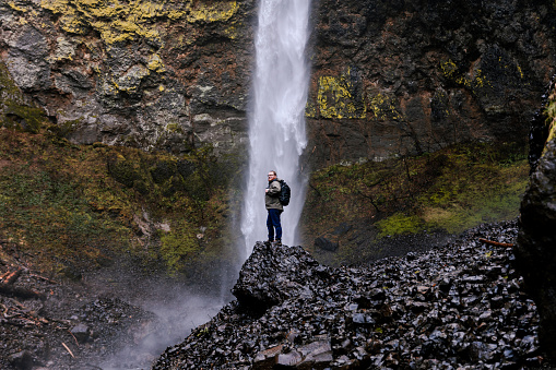 Young caucasian outdoorsman hiking with a backpack in a waterfall area in the Columbia River Gorge in the Pacific Northwest. Taken at Elowah Falls in Oregon.