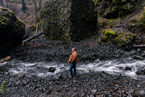 Young caucasian outdoorsman hiking with a backpack in a waterfall area in the Columbia River Gorge in the Pacific Northwest. Taken at Elowah Falls in Oregon.