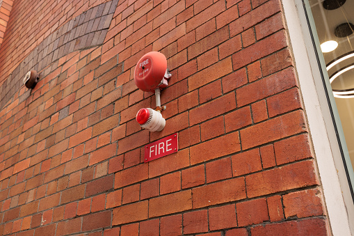 Looking up at an old fire alarm bell and light on a brick wall.