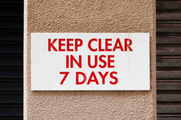 White and red sign on a wall to stop blockage of a driveway.