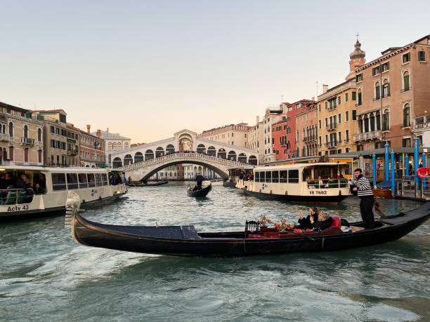 Venice, Italy - February 12, 2023: gondola and Rialto Bridge, oldest of the four bridges spanning Grand Canal in Venice in evening twilight