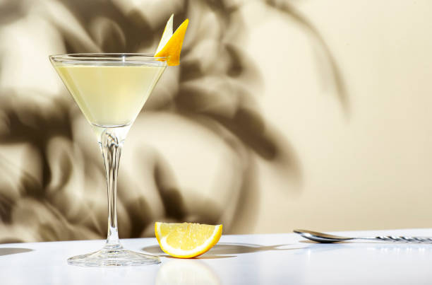 Vesper, classic alcoholic cocktail drink with dry gin, vodka, aperitif, lemon zest and ice. Light beige background, hard light, shadow pattern stock photo