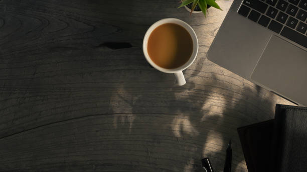 Laptop, cup of coffee and notebook on wooden table with sunlight. Top view with copy space.