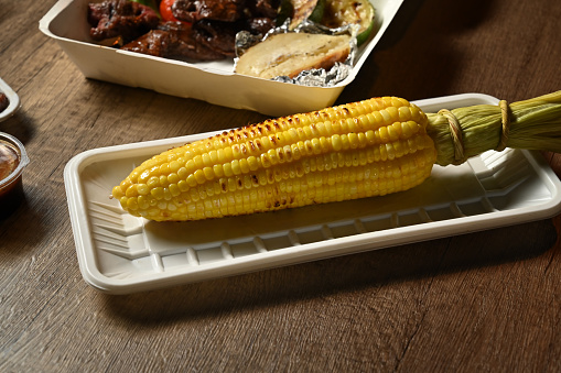 Grilled sweet corn in paper trays with grilled sliced beef steak over rustic table. Fast food take away, street food festival.