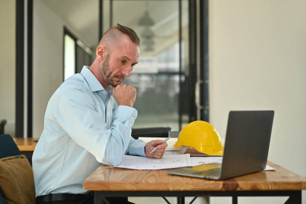 istock Focused caucasian man engineer looking at laptop screen and working on blueprint at workstation. 1468428605
