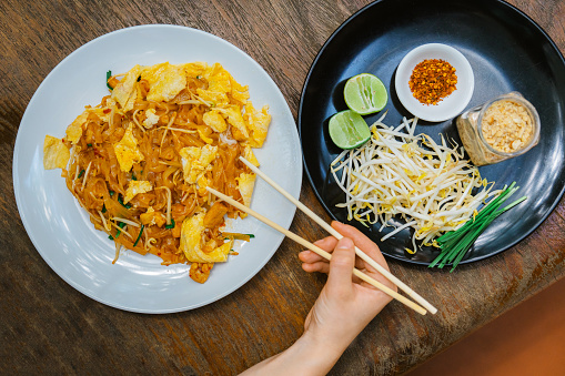 Directly above shot of woman hand with chopsticks getting pad Thai