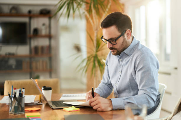 istock Male entrepreneur taking notes while working on laptop at home office. 1468437075