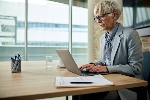 Senior businesswoman working on laptop in a modern office. Copy space.