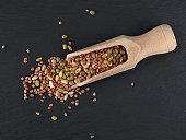 microgreen sprouts on wooden scoop on black slate background, top view of a mix of dry mungo, wheat and radish seeds