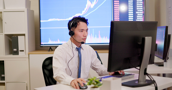 Asian male stock market analysts is working on customer service through computer and headsets in office