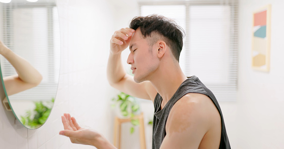 side view asian man standing in front of mirror is concerned about hair loss or alopecia