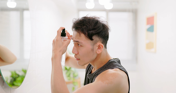 side view asian man use hair growing tonic in front of mirror