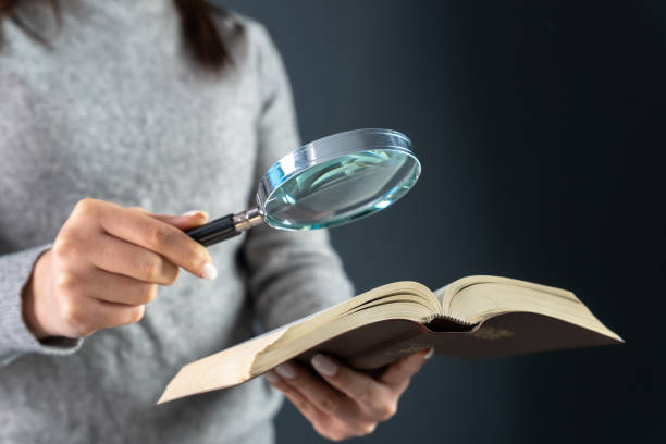 istock Woman looking at a book with a magnifying glass 1468443435