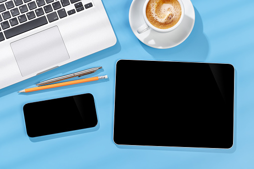 Tablet and smartphone with blank screen on business office desk. Flat lay workspace with sunny light and copy space