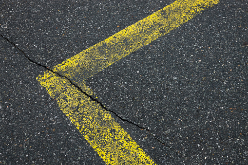 Yellow asphalt marklike a corner on a cracked grey street or road, texture as a background with space for text