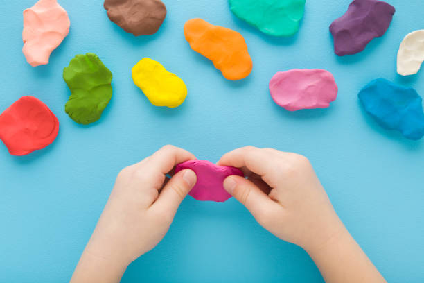 istock Baby boy hands holding and kneading modeling clay on light blue table background. Pastel color. Closeup. Top down view. Toddler development. Preparing material for making different colorful shapes. 1468459205
