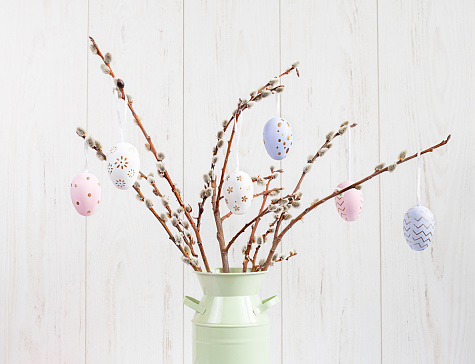 vase with willow branches and Easter eggs on a light wooden background
