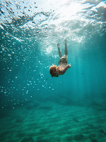 Young caucasian boy moving down underwater. He is swimming and diving in clear turquoise colored sea. Fish in the background. Kanali, Greece.