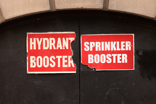 Sign on an old double door indicating hydrant and sprinkler boosters are inside.