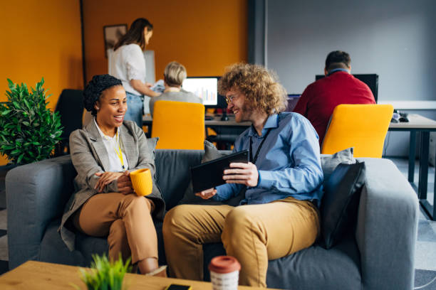 istock Two colleagues rest during a coffee break. They sit on a couch in the office, separated from other colleagues 1468464993
