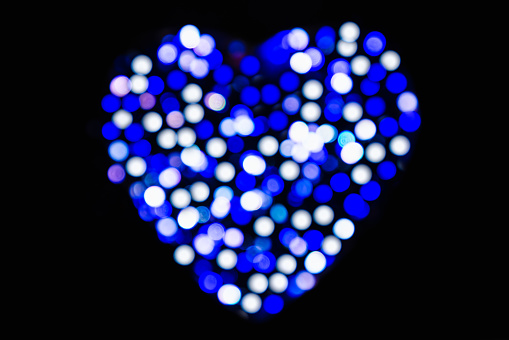 Blurred blue and white circles of light in the shape of a heart with bokeh effect on a black background for Valentines Day