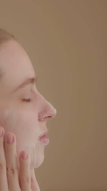 Young woman uses cleansing foam to wash her face, skin care procedure