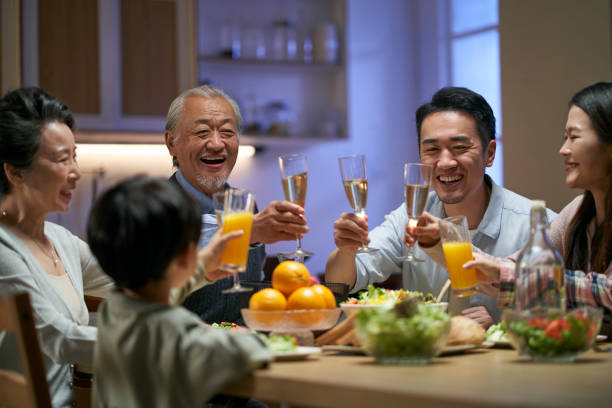 three generation asian family toasting while having dinner together stock photo