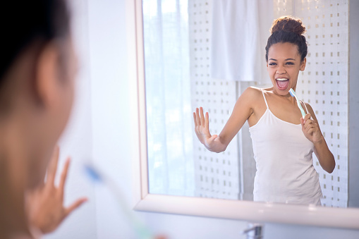 Bathroom, mirror and woman singing with a toothbrush before brushing her teeth for oral care. Happiness, fun and female dancing to karaoke music while doing fresh dental morning routine at home.