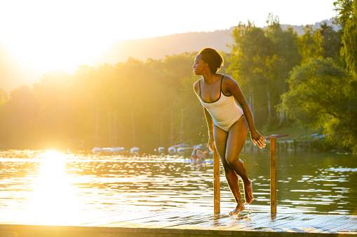 Young woman in white swimwear climbing ladder at lake.