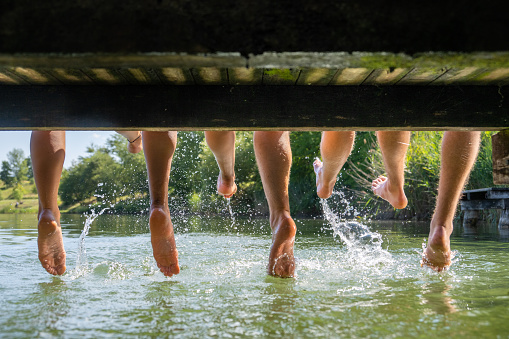 Low section of friends sitting on wooden pier at lake.